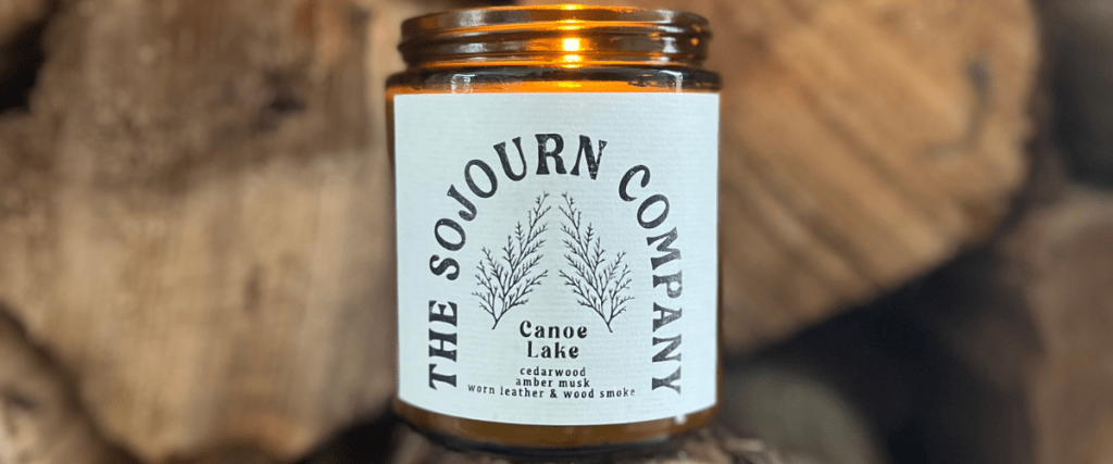 Sojourn Company candle lit and in front of logs